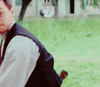 a man wearing a vest and white shirt is standing in a field