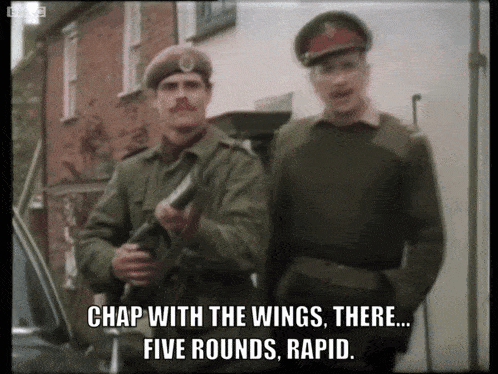 two men in military uniforms are standing next to each other and one of them says " chap with the wings there ... five rounds rapid "