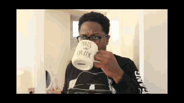 a man wearing glasses is drinking from a mug that says mais day i 'm ok