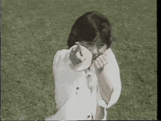 a woman in a white shirt is standing in the grass pointing at the camera