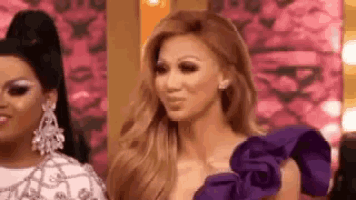a woman in a purple dress and earrings is standing next to another woman .