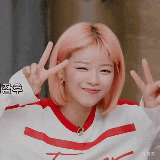 a girl with pink hair is giving a peace sign with her hands .
