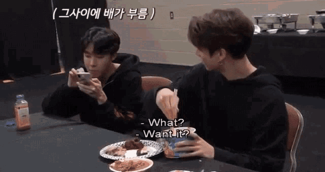 two young men are sitting at a table eating food and one of them is holding a cup that says what want it on it