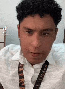 a man with curly hair is wearing a white shirt and a lanyard that says where .