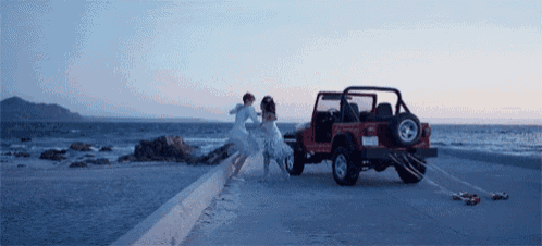 a couple of people are running towards a red jeep on the beach