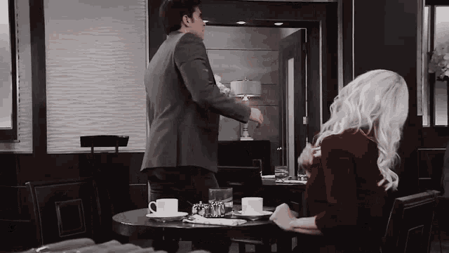 a man and a woman are sitting at a table with cups of coffee .