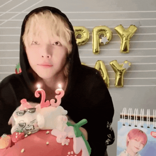a man in a black hoodie is holding a birthday cake with candles that say 23 on it
