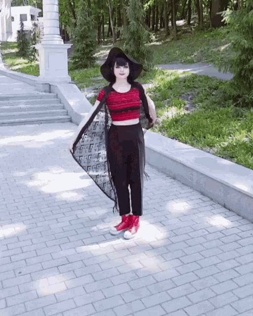 a woman wearing a black hat and a red crop top is standing on a sidewalk
