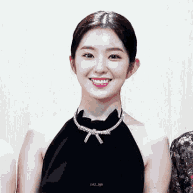 a woman wearing a black dress and a necklace smiles for the camera
