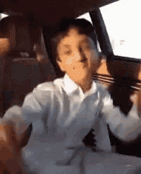 a young boy is sitting in the back seat of a car with his arms outstretched .