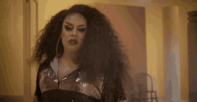 a drag queen with long curly hair is wearing hoop earrings