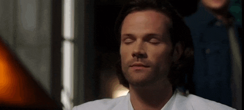 a man in a white shirt is sitting with his eyes closed in a room .