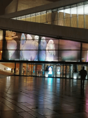 a man walking in front of a building with a large screen on the side of it