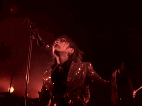 a woman in a sequined jacket sings into a microphone in a dark room