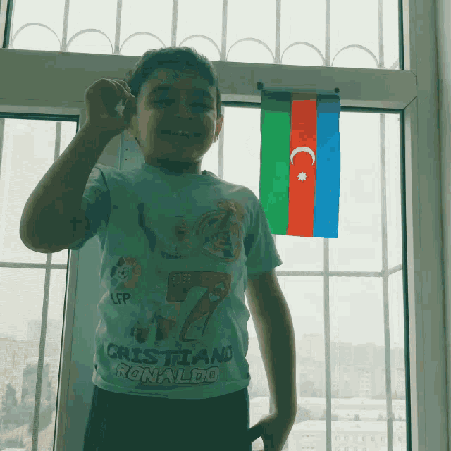 a boy wearing a shirt that says cristiano ronaldo stands in front of a window