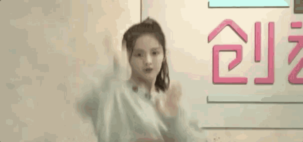 a young girl is standing in front of a wall with chinese writing on it and holding a pink object in her hand .
