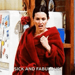 a woman in a red robe is standing in front of a refrigerator and giving a thumbs up .