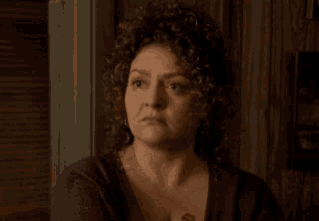 a woman with curly hair is wearing a purple shirt and has a tattoo on her chest .