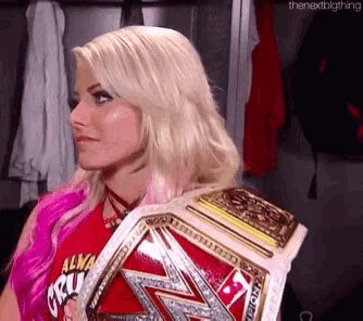 a woman in a red shirt is holding a wrestling championship belt on her shoulder .