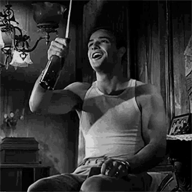 a man in a tank top is holding a bottle and laughing .