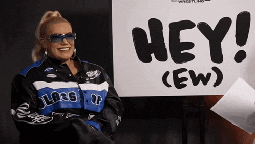 a woman wearing sunglasses is smiling in front of a sign that says hey