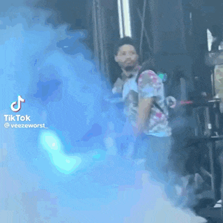 a man in a tie dye shirt is standing in front of a blue smoke bomb .