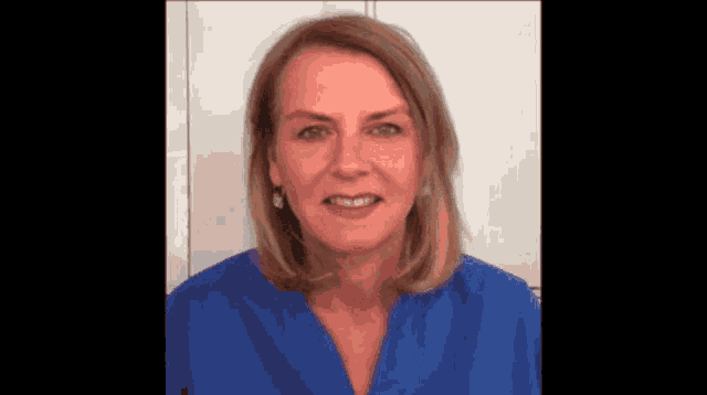 a woman wearing a blue shirt and earrings smiles at the camera