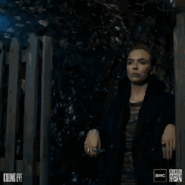 a woman in a black jacket is standing in front of a wooden fence with smoke coming out of it .