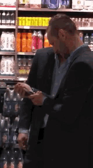 a man in a suit is looking at his phone in a grocery store aisle