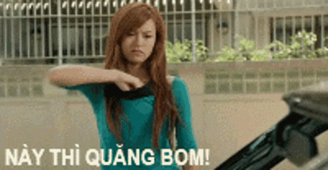a woman in a blue shirt is standing in front of a black car with the words nay thi quang bom written on the bottom