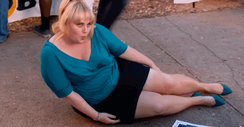 a woman in a blue top and black skirt sits on the sidewalk with her legs crossed