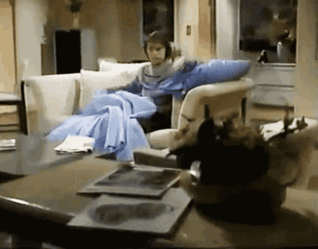a woman sits on a couch with a blue blanket