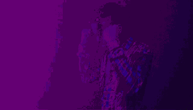 a man in a floral shirt adjusts his glasses in a dark room