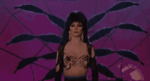 a woman in a bra and gloves is standing in front of a spider .