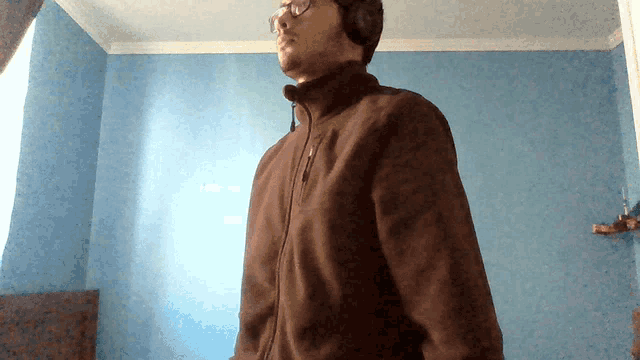 a man wearing headphones and a brown jacket stands in a room