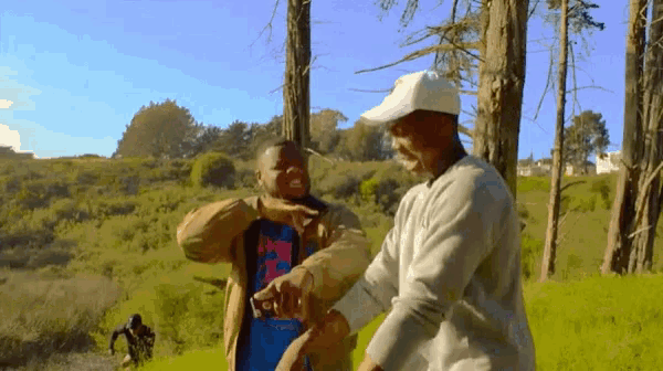two men are dancing in a field with trees in the background .