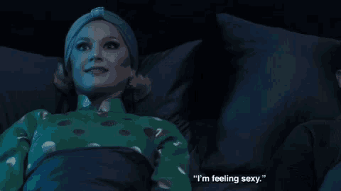 a woman in a green polka dot shirt is laying in bed with a man and says " i 'm feeling sexy "