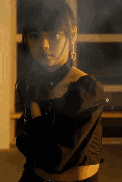 a woman wearing a black off the shoulder top and earrings stands with her arms crossed