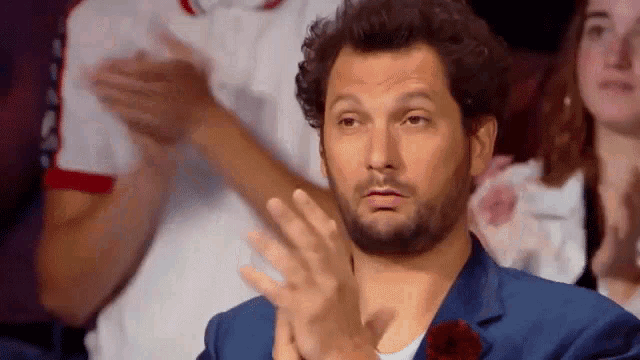 a man in a blue suit is clapping his hands while sitting in a crowd .