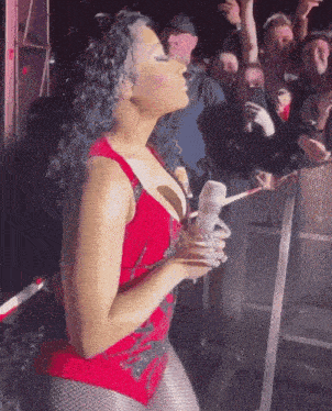 a woman in a red bodysuit is standing in front of a crowd of people holding a bottle of water .