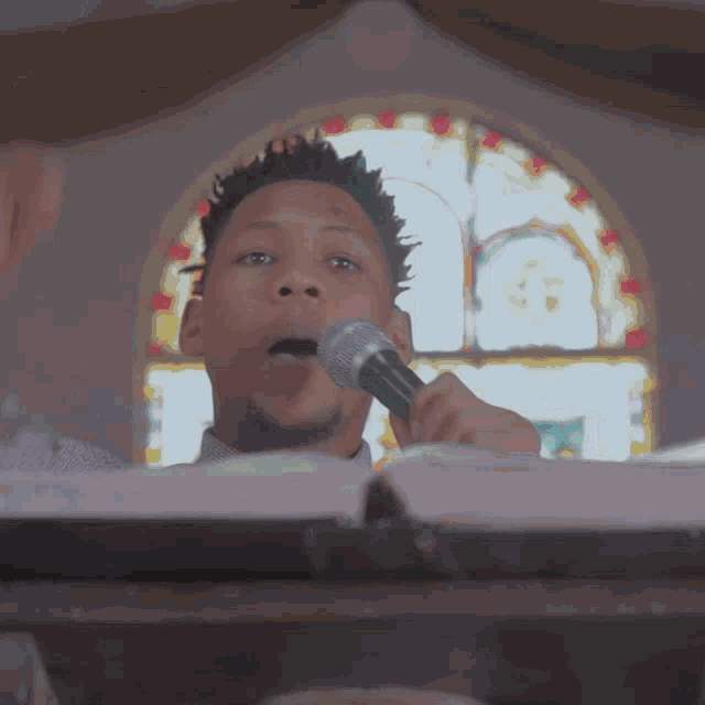 a man singing into a microphone with a stained glass window behind him