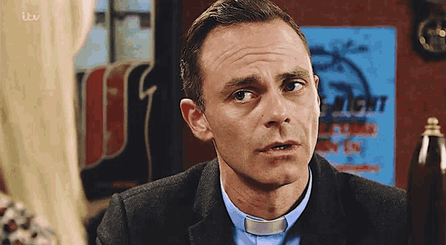 a man wearing a blue shirt and a clergy collar stands in front of a fright sign