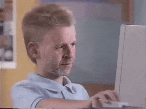a man with a mullet and beard is typing on a laptop computer .
