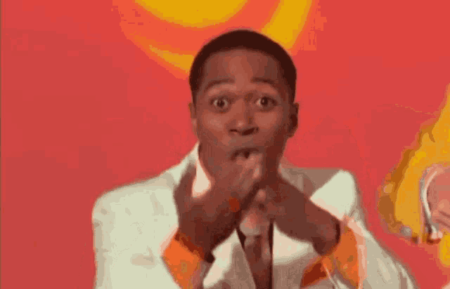 a man in a white suit and orange tie is making a surprised face