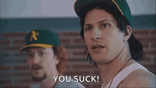 a man in a baseball cap is saying `` you suck '' while standing next to another man in a tank top .
