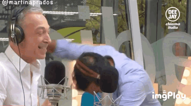 a man wearing headphones talks into a microphone while another man looks on