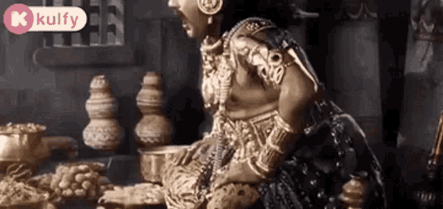 a statue of a woman in a gold dress is sitting at a table with a bowl of food .