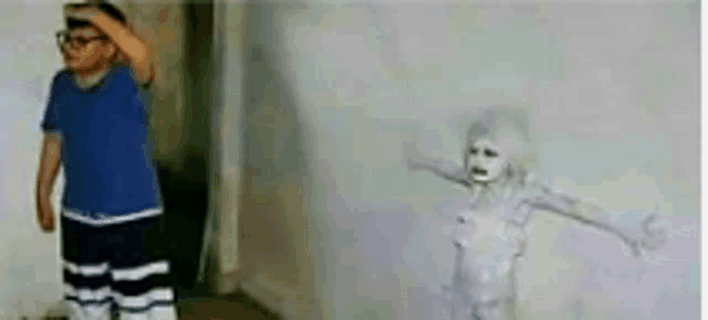a boy in a blue shirt is standing next to a drawing of a ghost .