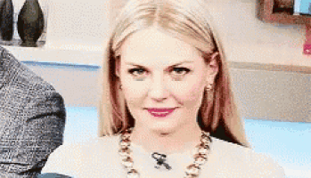 a woman wearing a necklace and earrings is sitting in front of a man .