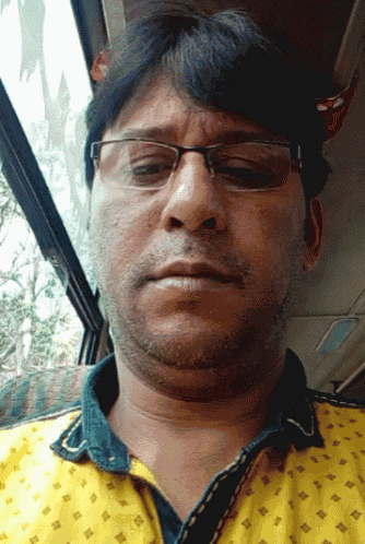 a man wearing glasses and a yellow shirt looks at the camera with his eyes closed